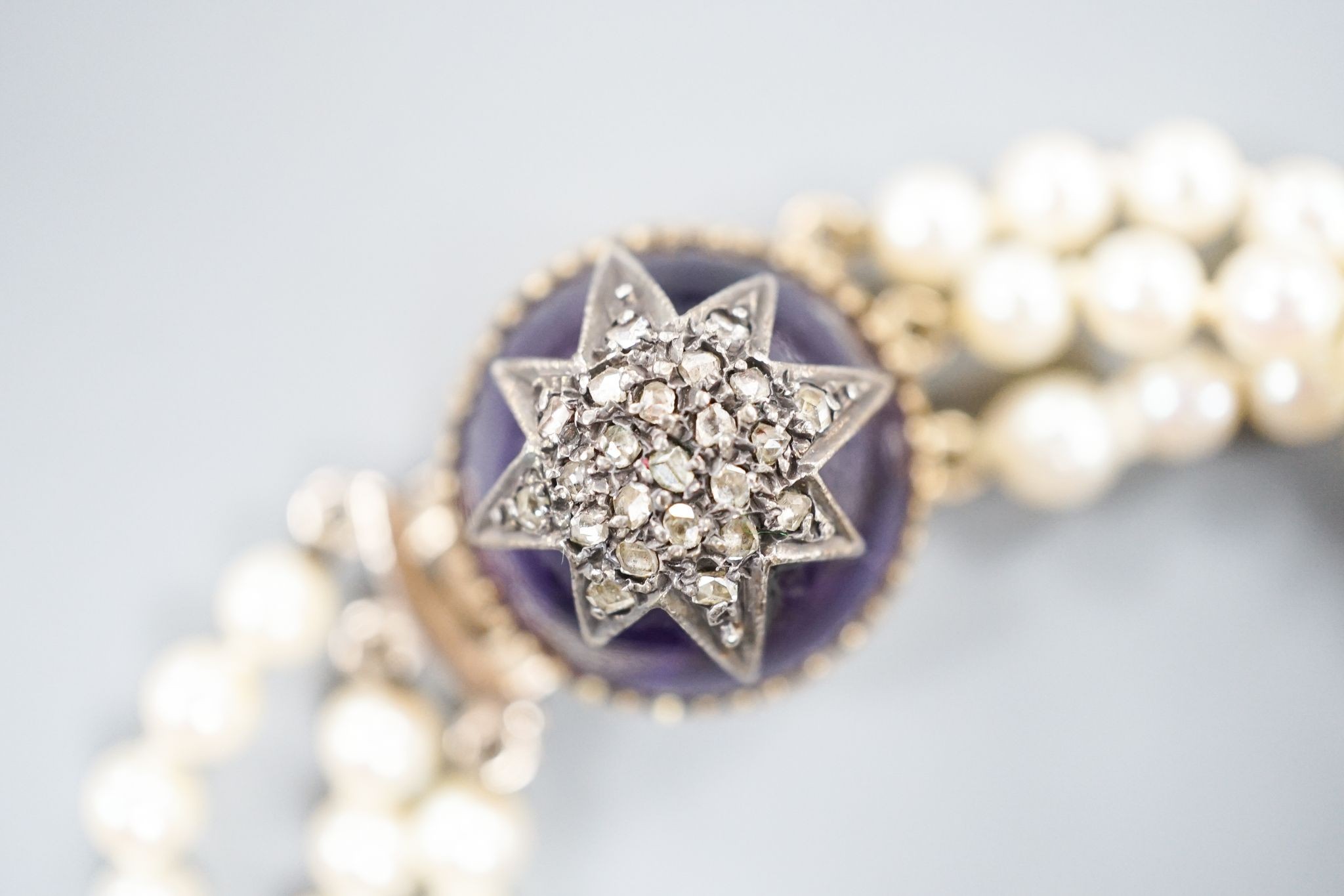 An early 20th century triple strand cultured? pearl bracelet, with rose cut diamond and cabochon amethyst set yellow metal clasp, 17.5cm, gross weight 21 grams.